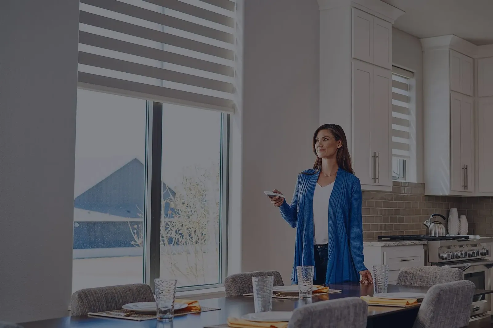 Homeowner lowering motorized layered shades in her kitchen with a remote
