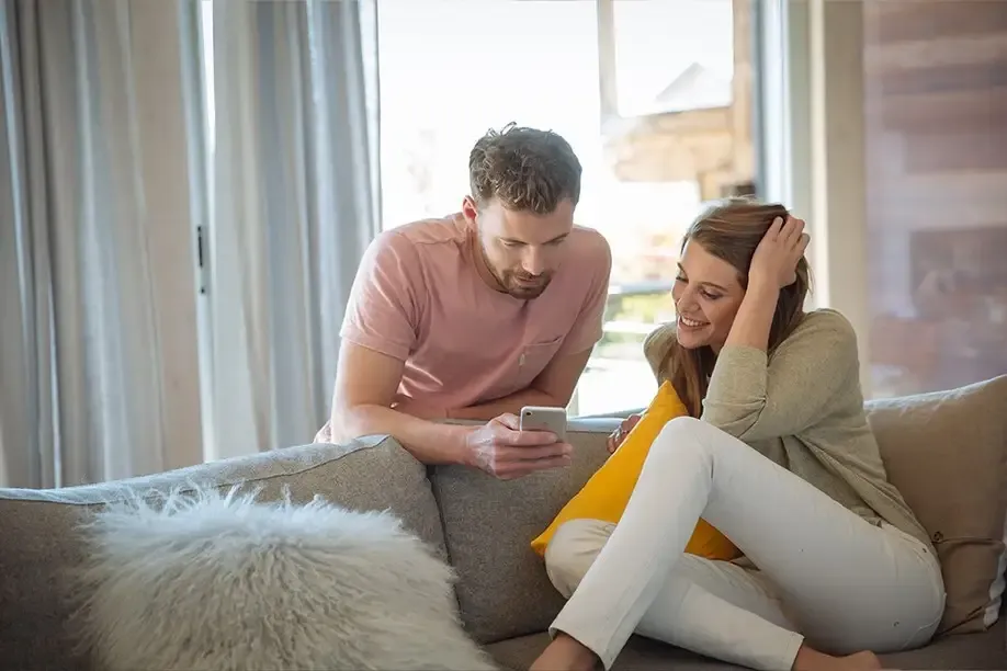 Couple on their sofa adjusting motorized drapery from a phone