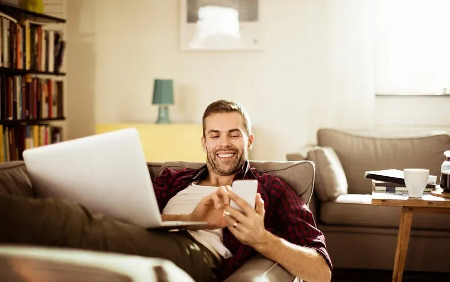 Man relaxing on a sofa using his phone with shades lowered behind him